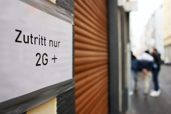 Ein Schild am Eingang einer Gaststätte mit geschlossenen Rollläden weist am 21. Januar 2022 auf die 2G-plus-Regel in Köln hin. Die Pandemie bestimmt weiterhin den Alltag.