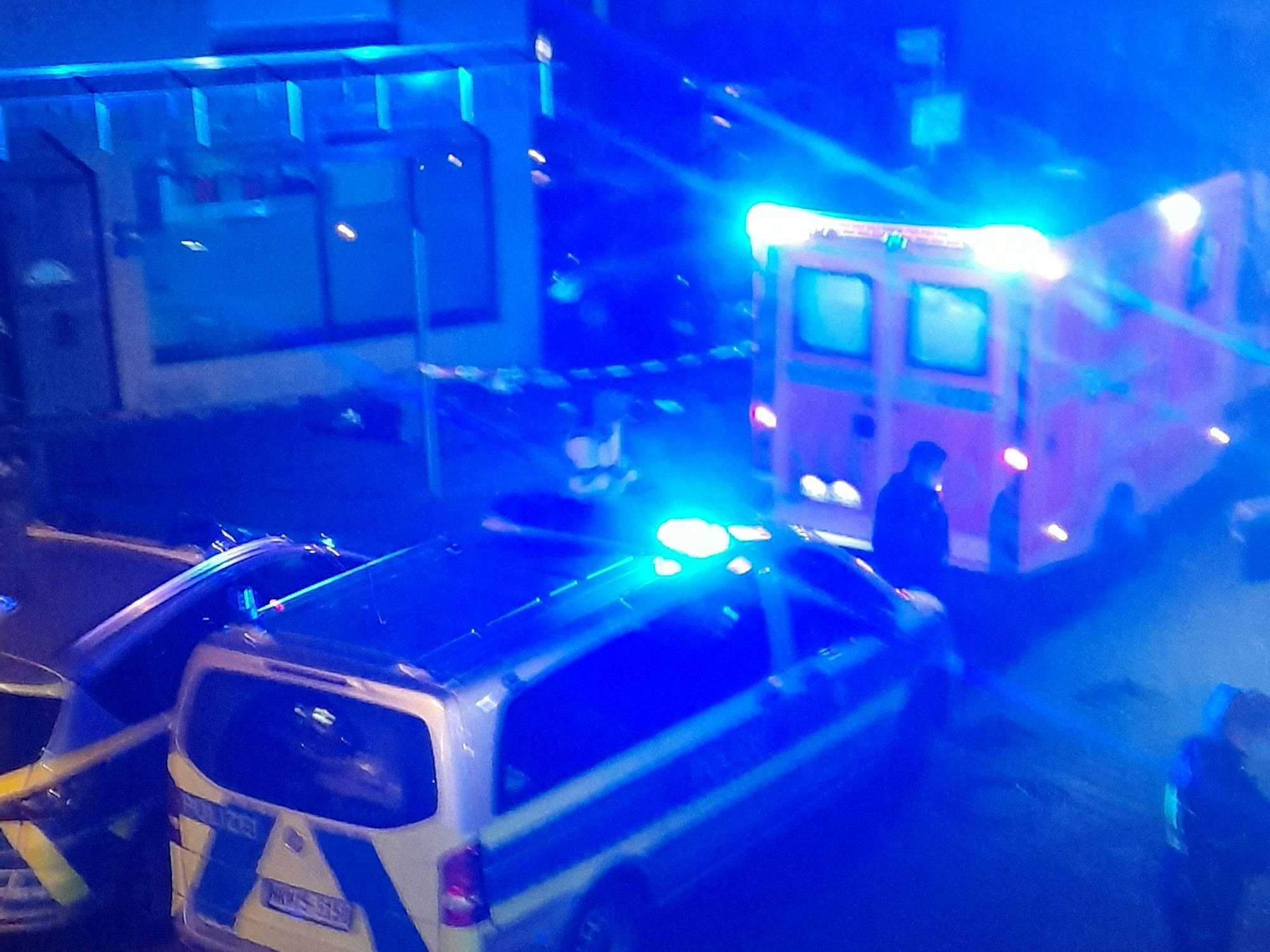 Rettungswagen und Polizeiautos mit Blaulicht stehen in einer Straße