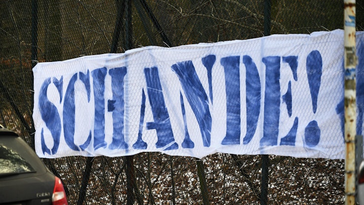 Ein weißes Banner mit der Aufschrift „Schande“ in blauen Buchstaben ist zu lesen.