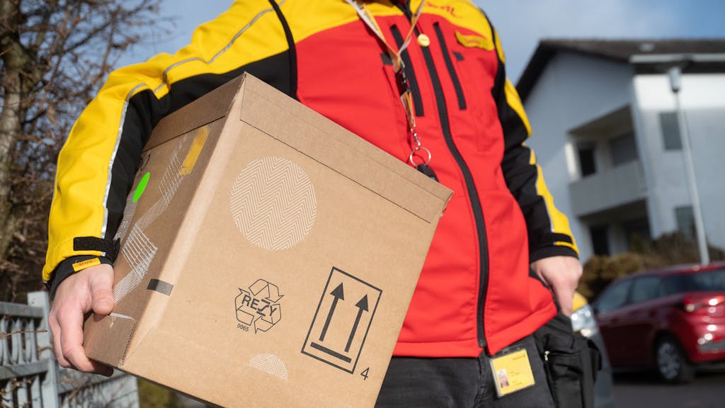 Ein DHL-Mitarbeiter trägt ein Paket unter seinem Arm. Foto vom 15. Dezember 2021.