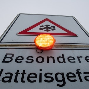 Ein Straßenschild warnt mit einer Blinkleuchte vor Glatteis