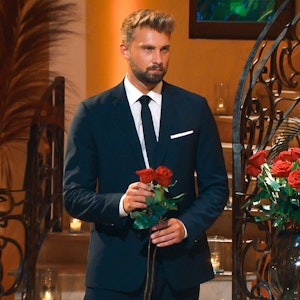 „Bachelor“ Dominik Stuckmann in einem schwarzen Anzug auf einem Foto aus der Show am 26. Januar 2022. In der Hand hält er zwei Rosen.