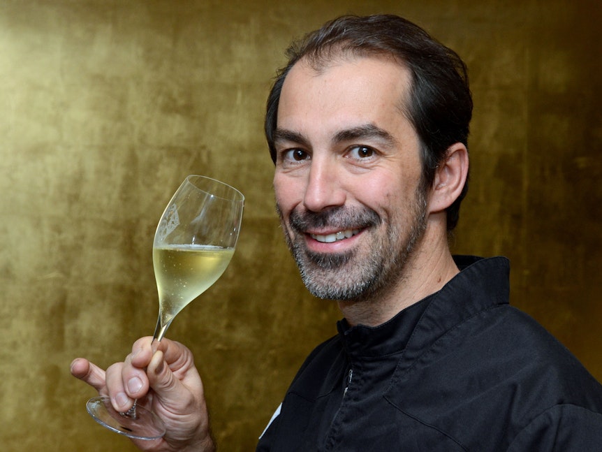 Spitzenkoch Volker Drkosch posiert mit einem Glas Champagner in der Hand.