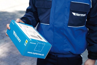 Ein Paketbote hält ein Päckchen der Hermes Logistik Gruppe in der Hand.