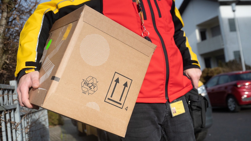 Ein DHL-Mitarbeiter trägt ein Paket unter seinem Arm. Das Foto entstand am 15. Dezember 2021.