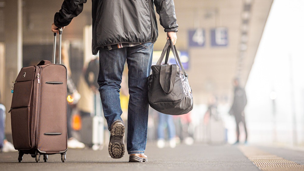 Ein Reisender geht mit seinem Koffer einen Bahnsteig entlang.