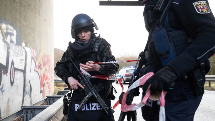 Zwei bewaffnete Polizeibeamte stehen mit Flatterband auf einer Straße.