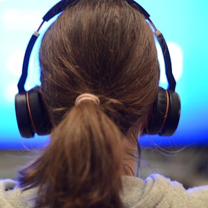 Eine Frau sitzt mit Kopfhörern vor einem Bildschirm.