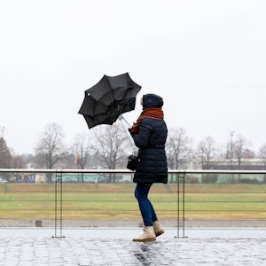 Im Rheinauhafen versucht eine Fußgängerin Ihren Schirm fest zu halten.