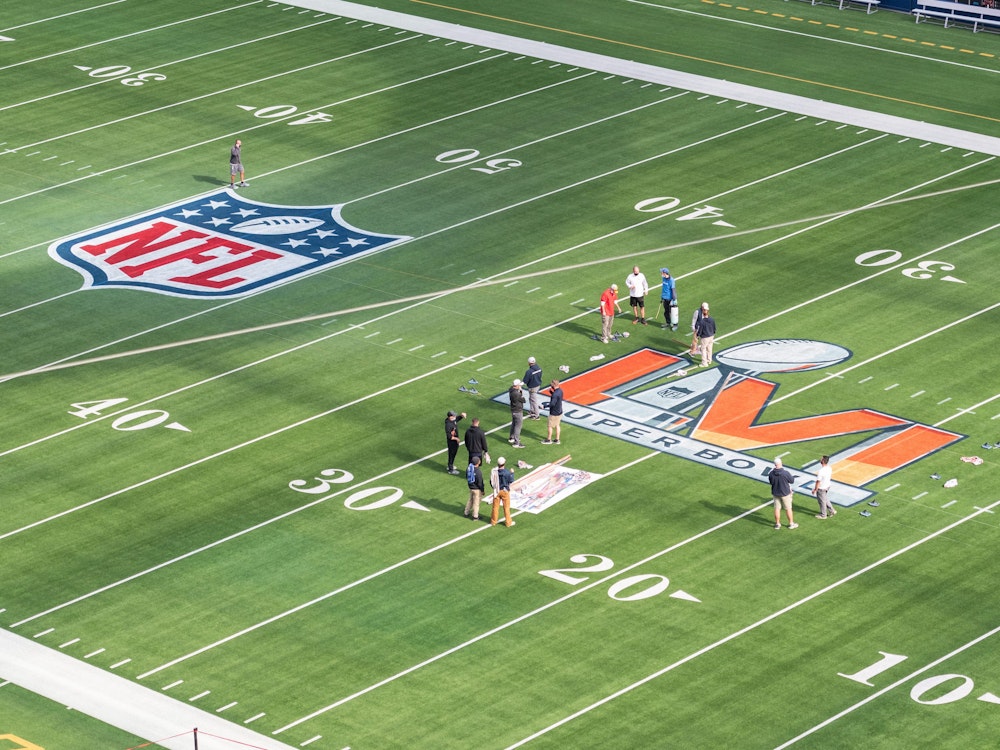 Arbeiter malen das Logo des Super Bowl LVI auf das Spielfeld im SoFi Stadium.