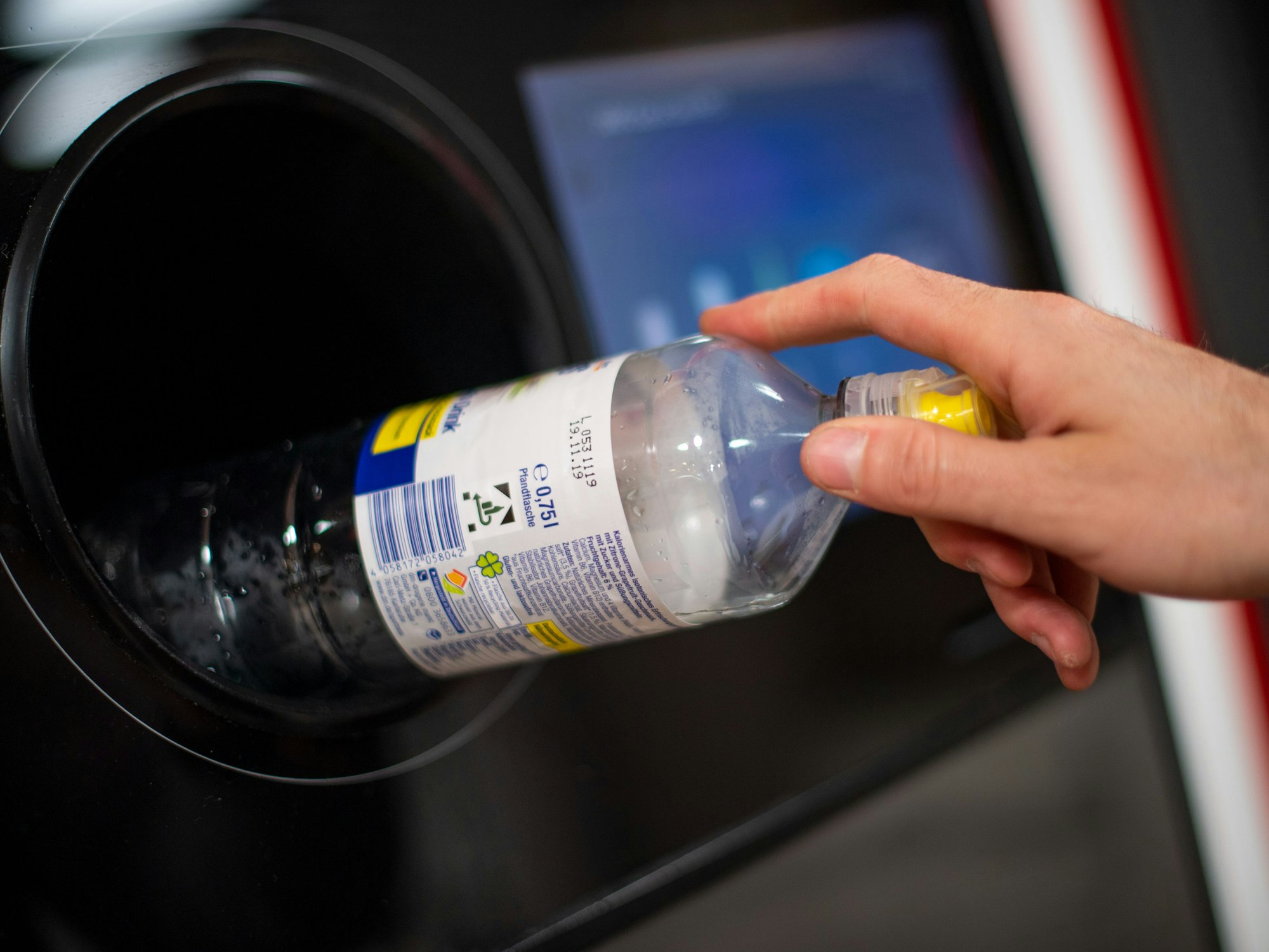 Eine Person wirft eine Plastikflasche in einen Pfandautomaten.