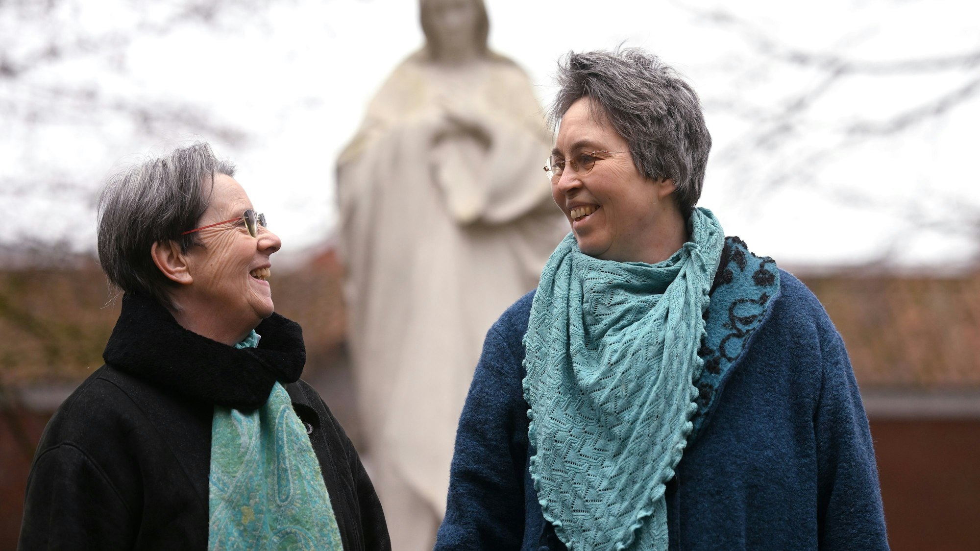 Queer in Church: Monika Schmelter (links) und Marie Kortenbusch vor einer Marienstatue eines Klosters. Die beiden sind ein Paar.