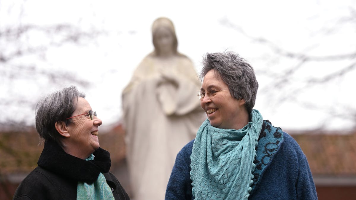 Queer in Church: Monika Schmelter (links) und Marie Kortenbusch vor einer Marienstatue eines Klosters. Die beiden sind ein Paar.