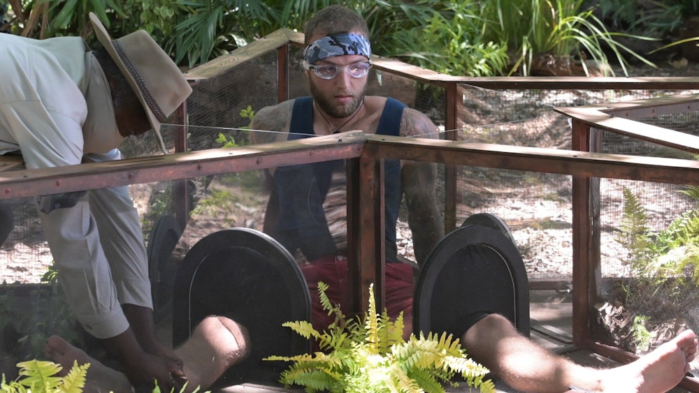 Das Foto zeigt Dschungelcamp-Finalist Filip Pavlovic während einer Dschungelprüfung auf dem Boden sitzend mit einer Schutzbrille