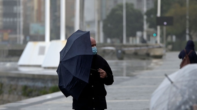 Ein Mann schützt sich vor Wind und Regen mit einem Regenschirm. Das Bild entstand am 8. Dezember 2021.