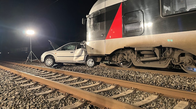 Ein Auto steht auf Gleisen vor einem Zug.