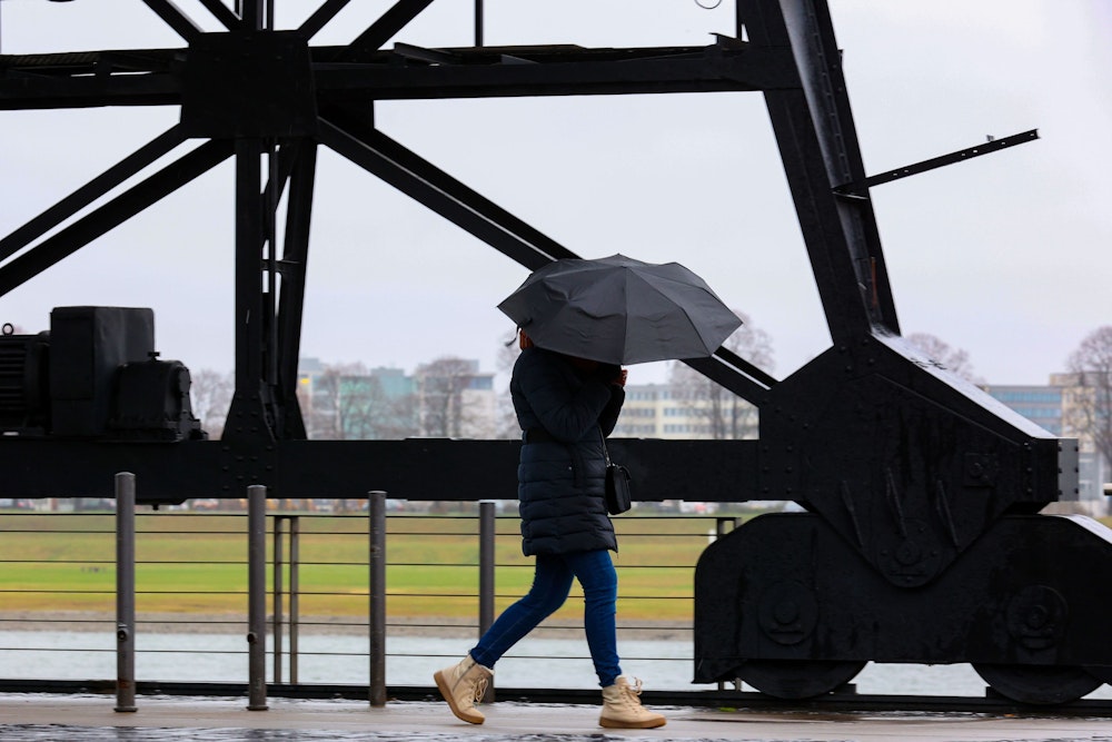 Köln: Im Rheinauhafen versucht eine Fußgängerin Ihren Schirm fest zu halten. Anhaltendes stürmisches Regenwetter über Köln.