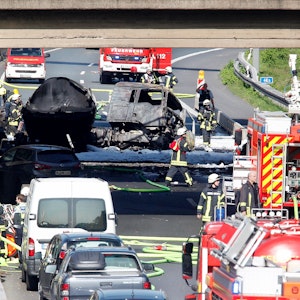 Nordrhein-Westfalen, Mülheim: Feuerwehrleute stehen an dem ausgebrannten Tanklaster auf der A40.