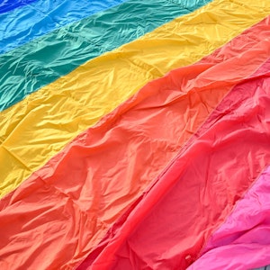 Auf dem Boden liegt eine große LGBTQI+-Flagge und jemand steht darauf.