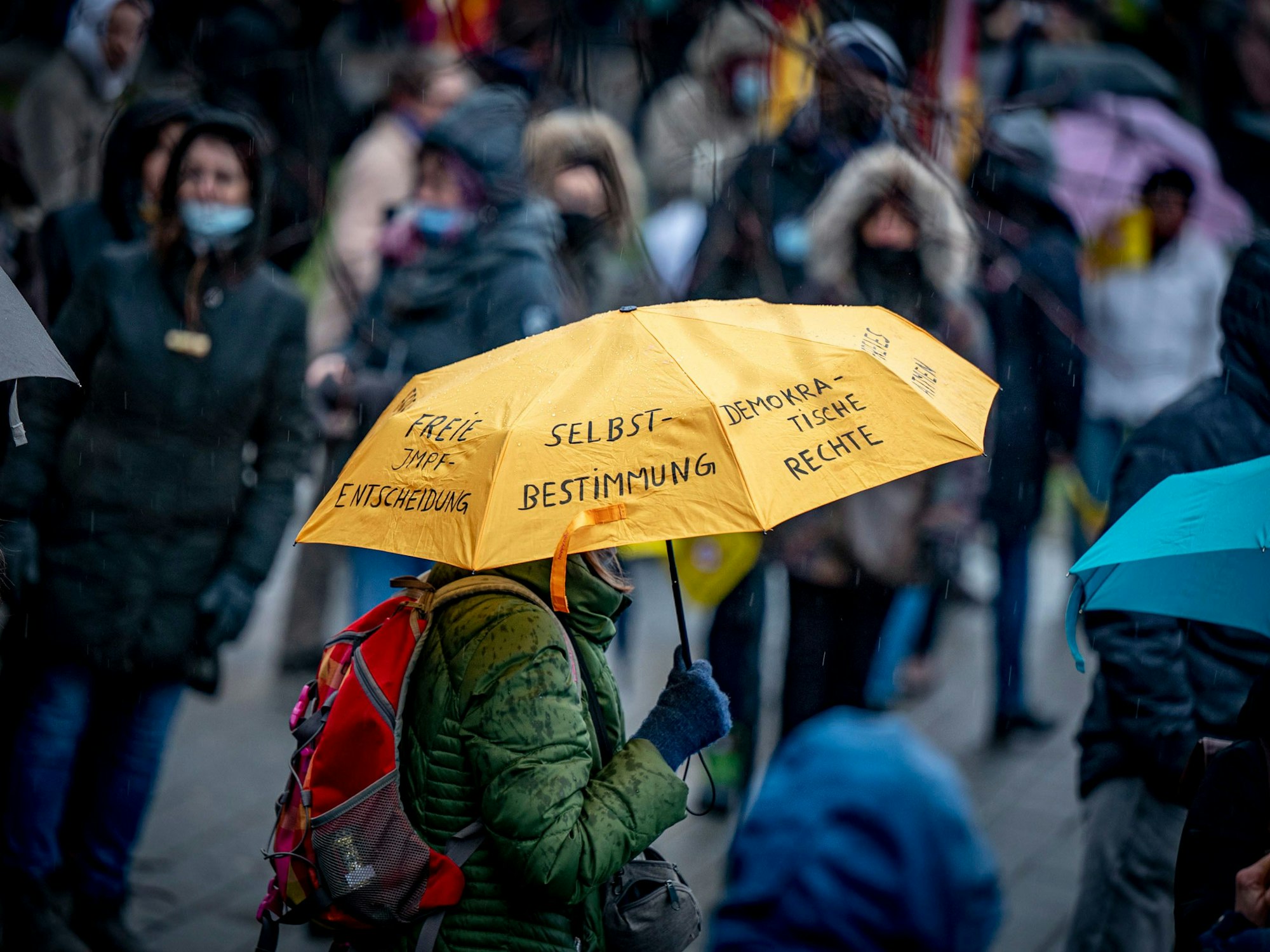 Gegner der Corona-Maßnahmen nehmen an einer Demonstration teil, eine Person hält einen Regenschirm, auf dem u.a. „Selbstbestimmung“ und „Demokratische Rechte“ steht.