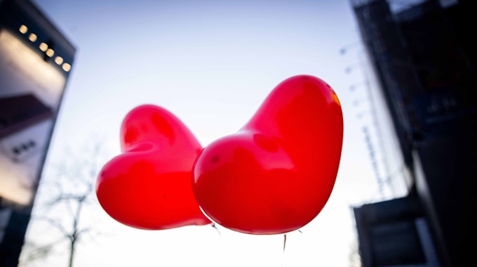 Zwei rote Ballons in Herzform fliegen in der Luft.