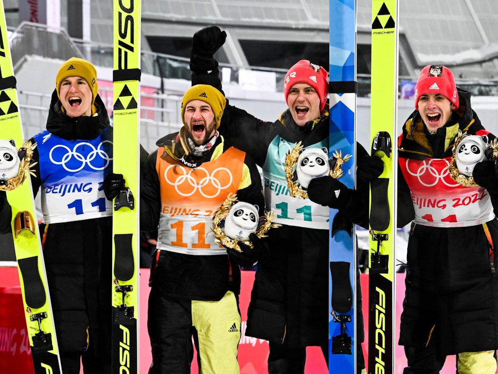 Die deutschen Skispringer Constantin Schmid, Stephan Leyhe, Markus Eisenbichler und Karl Geiger jubelnd auf dem Podium nach dem Gewinn der Bronzemedaille im Team am 14. Februar 2022.