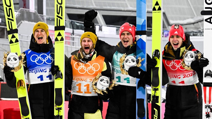 Die deutschen Skispringer Constantin Schmid, Stephan Leyhe, Markus Eisenbichler und Karl Geiger jubelnd auf dem Podium nach dem Gewinn der Bronzemedaille im Team am 14. Februar 2022.