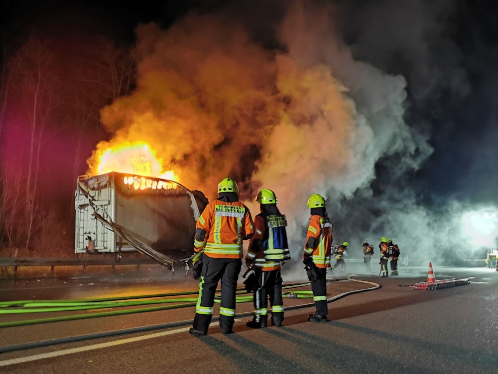Feuerwehrleute vor einem brennenden Lkw auf der Autobahn.