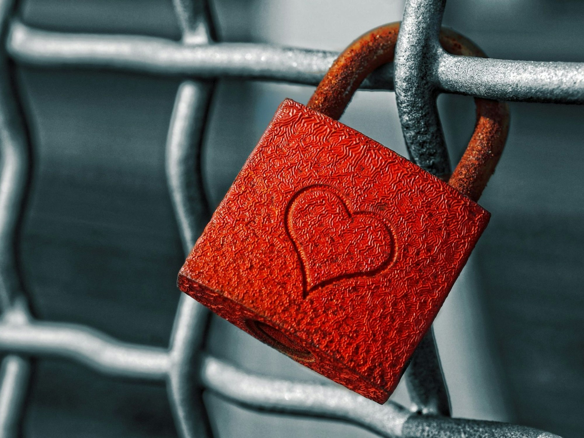Ein rotes Herzschloss hängt an einem Zaun.