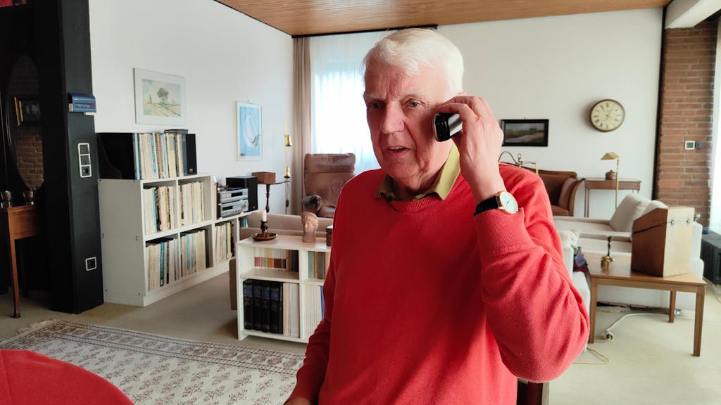 Rentner Herbert telefoniert in seinem Wohnzimmer.