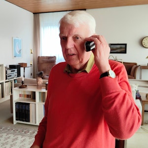 Rentner Herbert telefoniert in seinem Wohnzimmer.