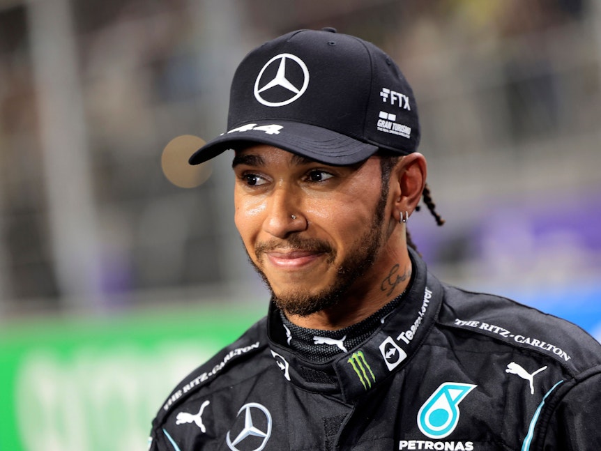 Mercedes-Fahrer Lewis Hamilton lächelt im Mercedes-Outfit.