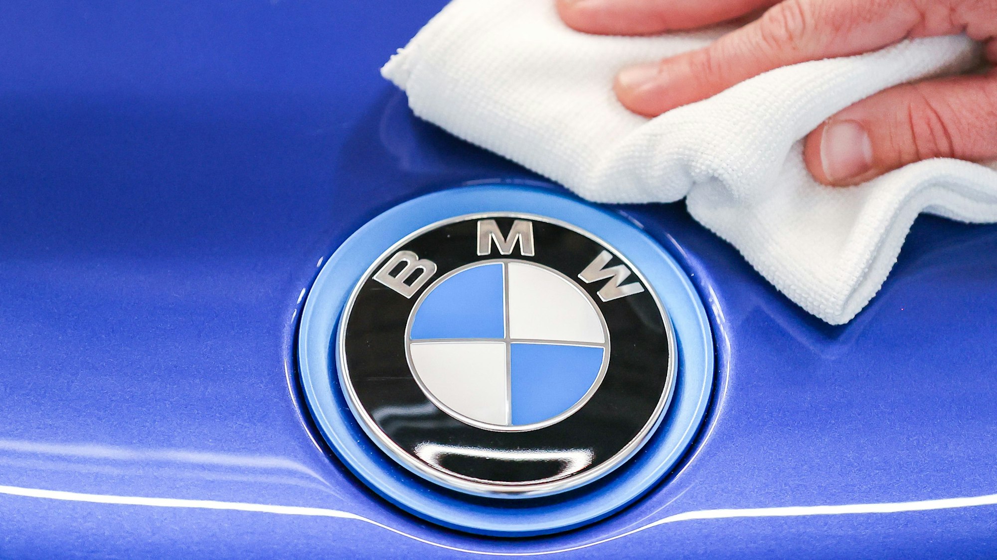 Ein Mitarbeiter von BMW poliert mit einem Tuch das Logo von einem BMW i8.