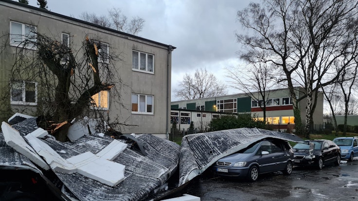 Teile eines vom Sturm Ylenia abgedeckten Flachdaches liegen auf einer Straße und auf geparkten Autos.