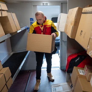 Ein DHL-Mitarbeiter sortiert in seinem Transporter Pakete für die nächsten Zustellungen.