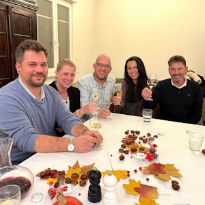 Die Das Perfekte Dinner-Kandidaten Marcus, Simone, Gastgeber Andreas, Sabrina und Jürgen sitzen an Andreas Tisch und lächeln.