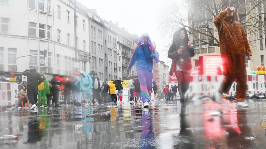 Verkleidete Karnevalisten gehen über eine regennasse Straße.