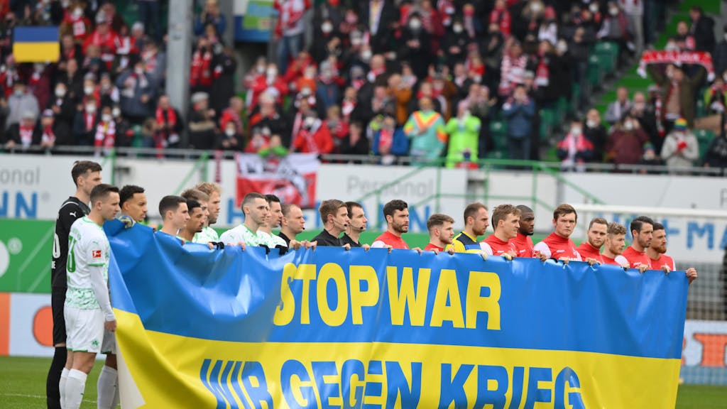 Die Spieler von Greuther Fürth und dem 1. FC Köln halten ein Banner hoch.