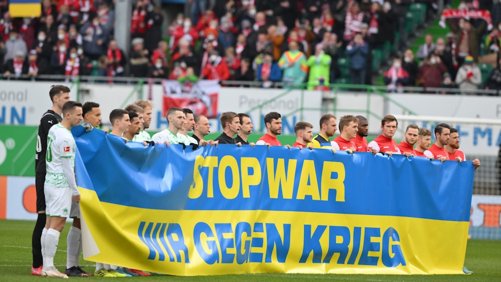 Die Spieler von Greuther Fürth und dem 1. FC Köln halten ein Banner hoch.