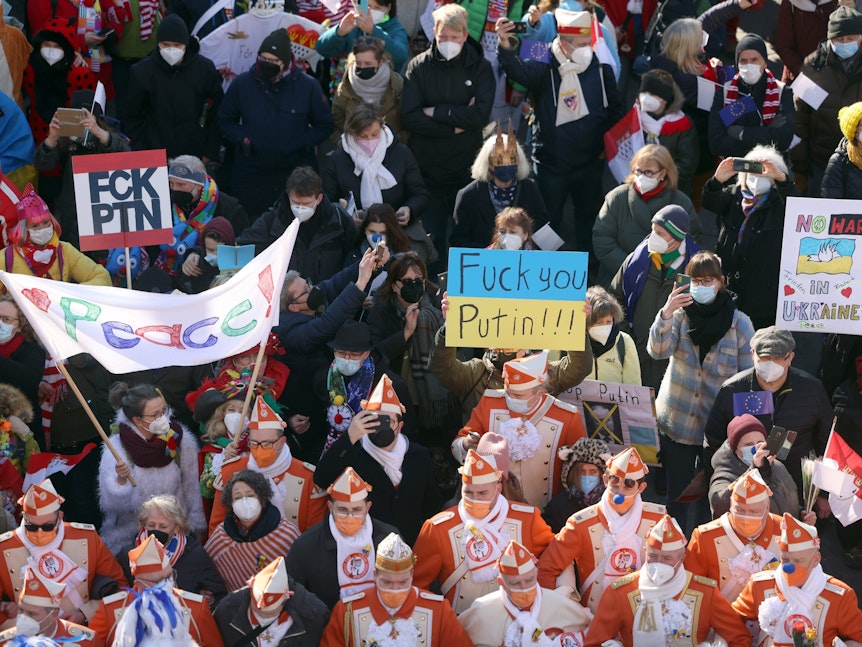 Zahlreiche Karnevalisten haben sich am Rosenmontag am Chlodwigplatz versammelt und halten ein Schild mit der Aufschrift „Fuck you Putin“.