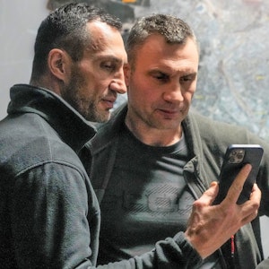 Vitali Klitschko (r), Bürgermeister von Kyjiw und ehemaliger Box-Profi, und sein Bruder Wladimir Klitschko, ebenfalls ehemaliger Box-Profi, schauen auf ein Smartphone im Rathaus in Kyjiw.