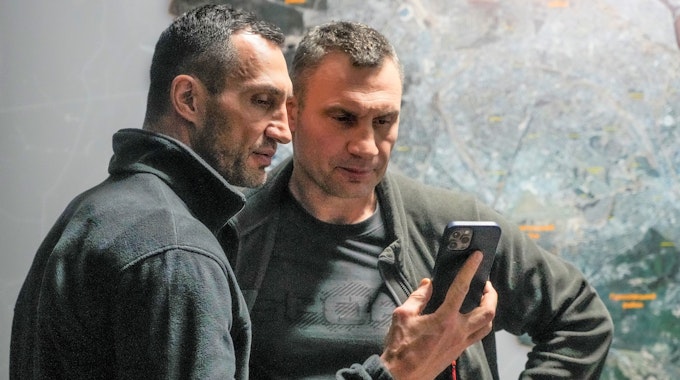 Vitali Klitschko (r), Bürgermeister von Kyjiw und ehemaliger Box-Profi, und sein Bruder Wladimir Klitschko, ebenfalls ehemaliger Box-Profi, schauen auf ein Smartphone im Rathaus in Kyjiw.