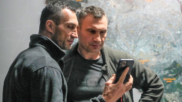 Vitali Klitschko (r), Bürgermeister von Kiew und ehemaliger Box-Profi, und sein Bruder Wladimir Klitschko, ebenfalls ehemaliger Box-Profi, schauen auf ein Smartphone im Rathaus in Kiew.
