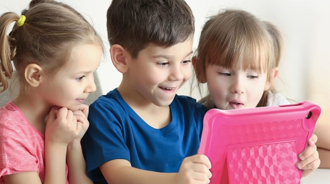 Drei Kinder gucken aufgeregt auf ein pinkes Kinder-Tablet.