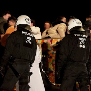 Drei Polizisten stehen vor feiernden Jugendlichen.