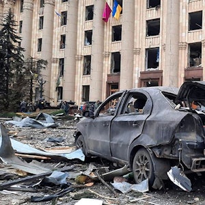Ein zerstörtes Auto steht vor dem beschädigten Rathausgebäude von Charkiw