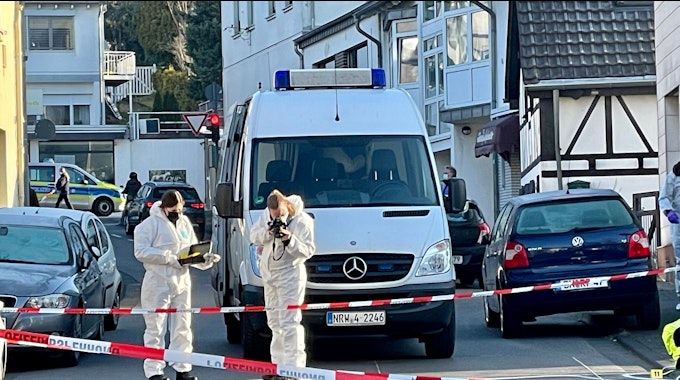 Die Kreuzherrenstraße in Bonn ist mit Polizei-Flatterband abgesperrt, zwei Beamtinnen sichern Spuren. Ein Einsatzfahrtzeug der Polizei steht an der Absperrung.