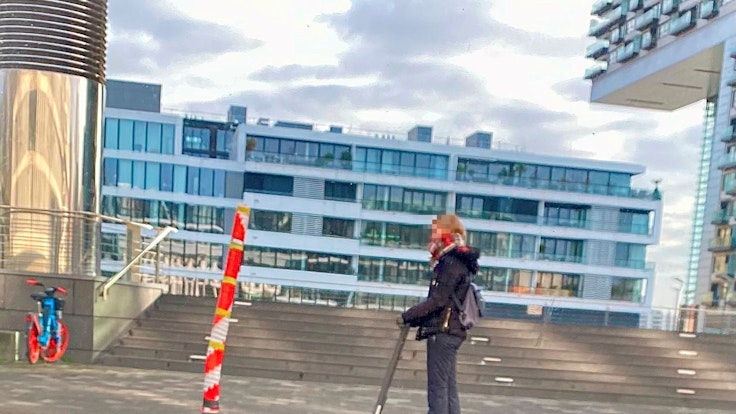 Ein Mast mitten auf dem Gehweg am Rheinauhafen in Köln, fotografiert vor wenigen Tagen. Eine Person fährt mit einem Roller daran vorbei.