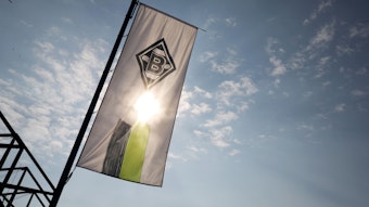 Eine Fahne mit dem Logo von Borussia Mönchengladbach weht am Borussia-Park. Im Hintergrund scheint die Sonne.