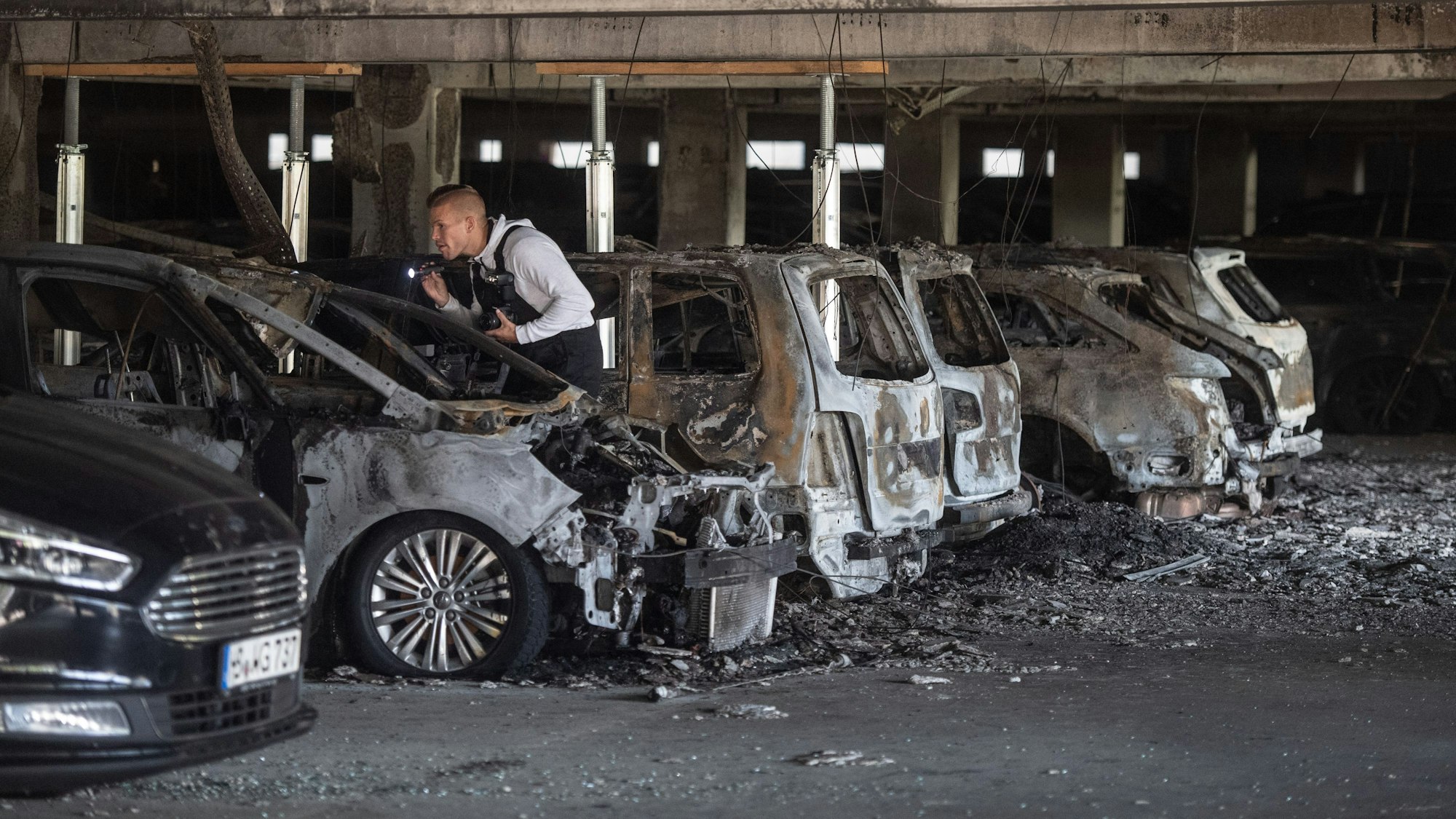 Ein Sachverständiger untersucht in einem Parkhaus ausgebrannte Autos.
